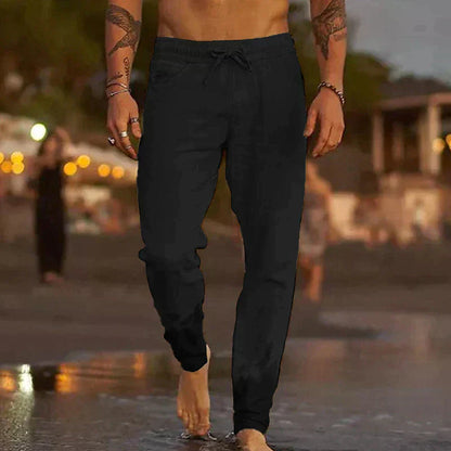 Uomo che cammina sulla spiaggia al tramonto indossando pantaloni neri casual. Moda maschile estiva, abbigliamento comodo per serate estive.