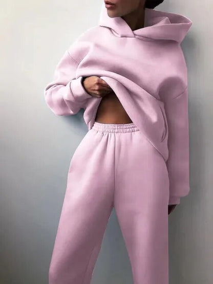 Donna in tuta sportiva rosa pastello, felpa con cappuccio e pantaloni comodi. Moda casual, abbigliamento sportivo trendy, stile rilassato.