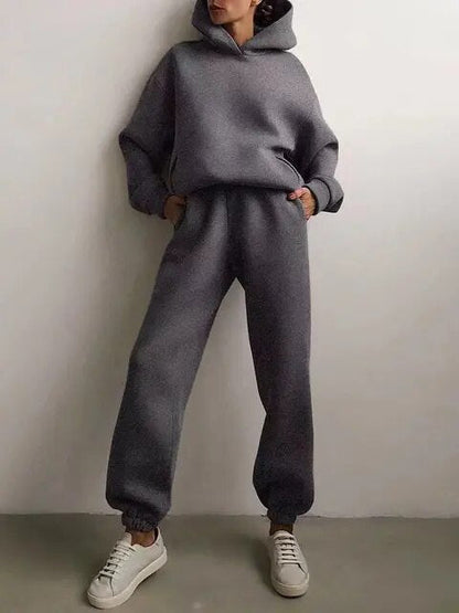 Donna in tuta grigia con cappuccio, pantaloni larghi e sneakers bianche. Moda casual, abbigliamento comodo, stile urbano.