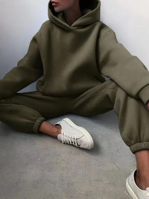 Donna seduta con felpa e pantaloni tuta verde oliva, scarpe da ginnastica bianche. Abbigliamento casual, moda streetwear, comfort urbano.