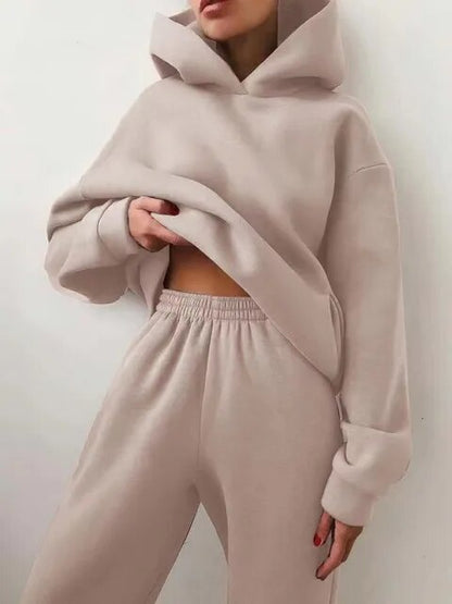 Donna in tuta beige, felpa con cappuccio e pantaloni larghi. Moda casual, abbigliamento comodo, stile minimalista.