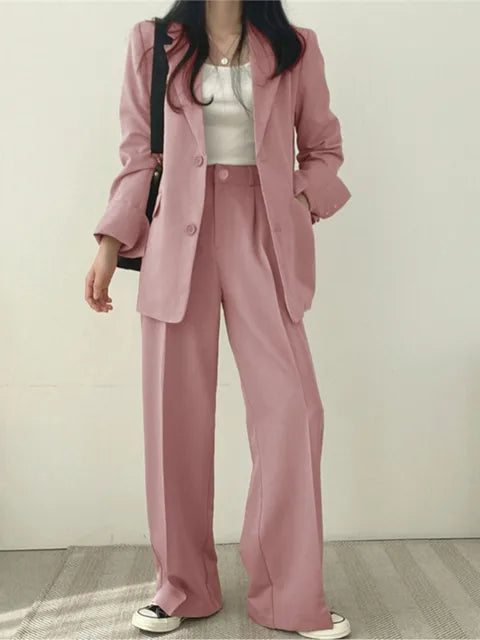 Donna in completo rosa elegante, giacca e pantaloni larghi, indossa sneakers bianche e nere, borsa a tracolla nera. Moda femminile casual chic.