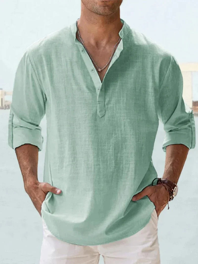 Camicia uomo verde menta in lino, maniche lunghe arrotolate, scollo a V con bottoni, stile casual estivo, indossata con pantaloni bianchi.