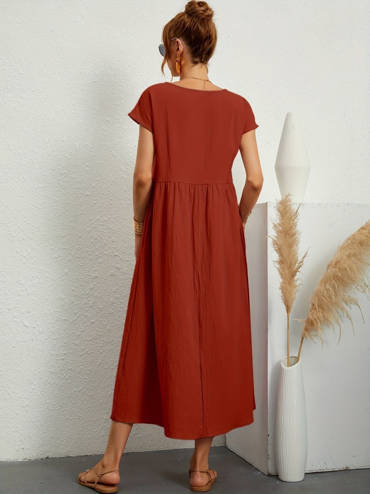 Donna di spalle con abito lungo rosso, sandali beige, accanto a vaso bianco con pampas. Stile estivo, moda casual, abbigliamento femminile.
