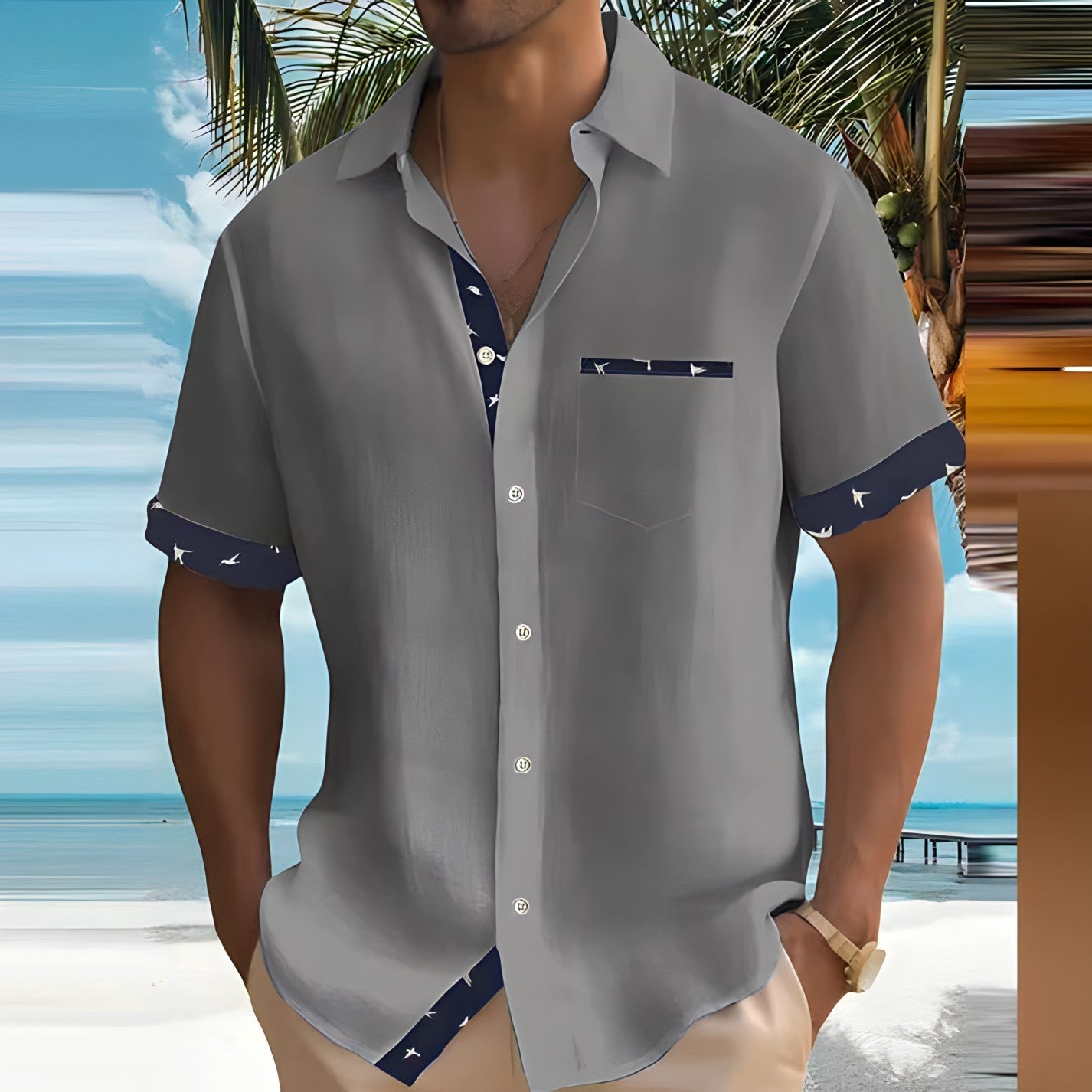 Camicia estiva da uomo grigia con dettagli blu, indossata su spiaggia tropicale. Moda casual, abbigliamento estivo, stile vacanza.