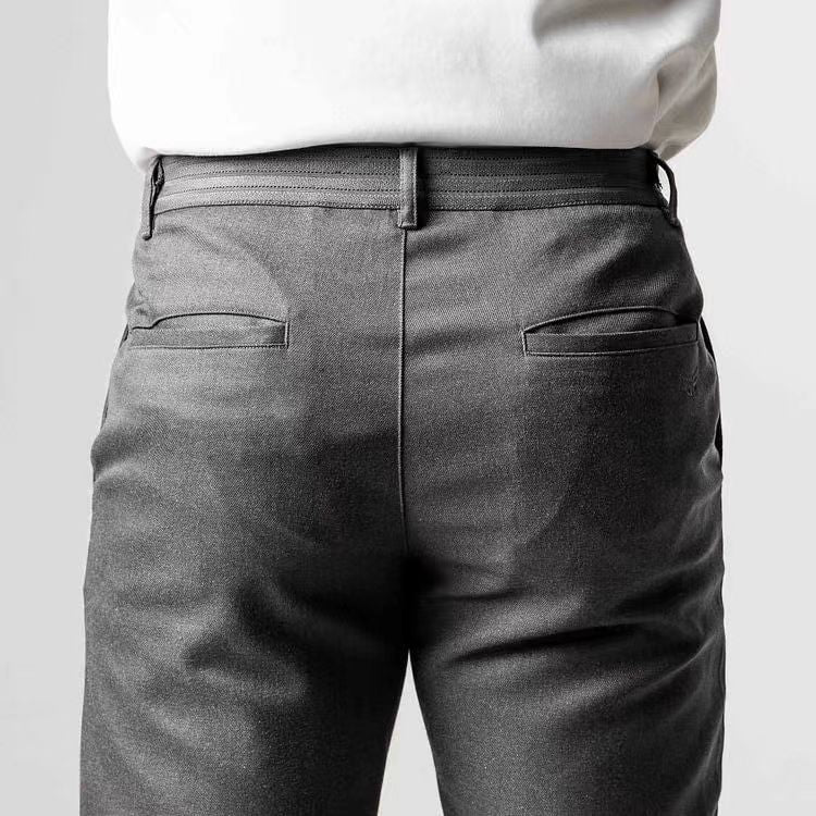 Pantaloni eleganti grigi da uomo, vista posteriore, con tasche posteriori a filetto. Tessuto liscio, abbinato a camicia bianca. Moda maschile formale.