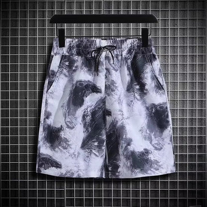 Pantaloncini sportivi uomo con stampa astratta bianco e nero, elastico in vita, tasche laterali, appesi su griglia metallica. Moda casual estiva.