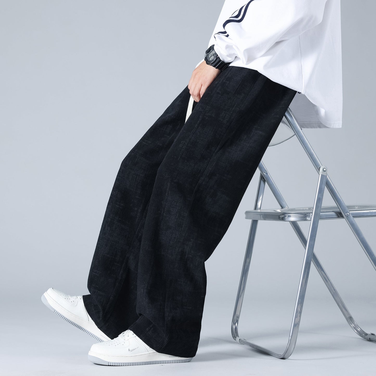 Pantaloni larghi neri uomo, stile casual, indossati con scarpe bianche e camicia bianca, moda streetwear, seduto su sedia pieghevole.