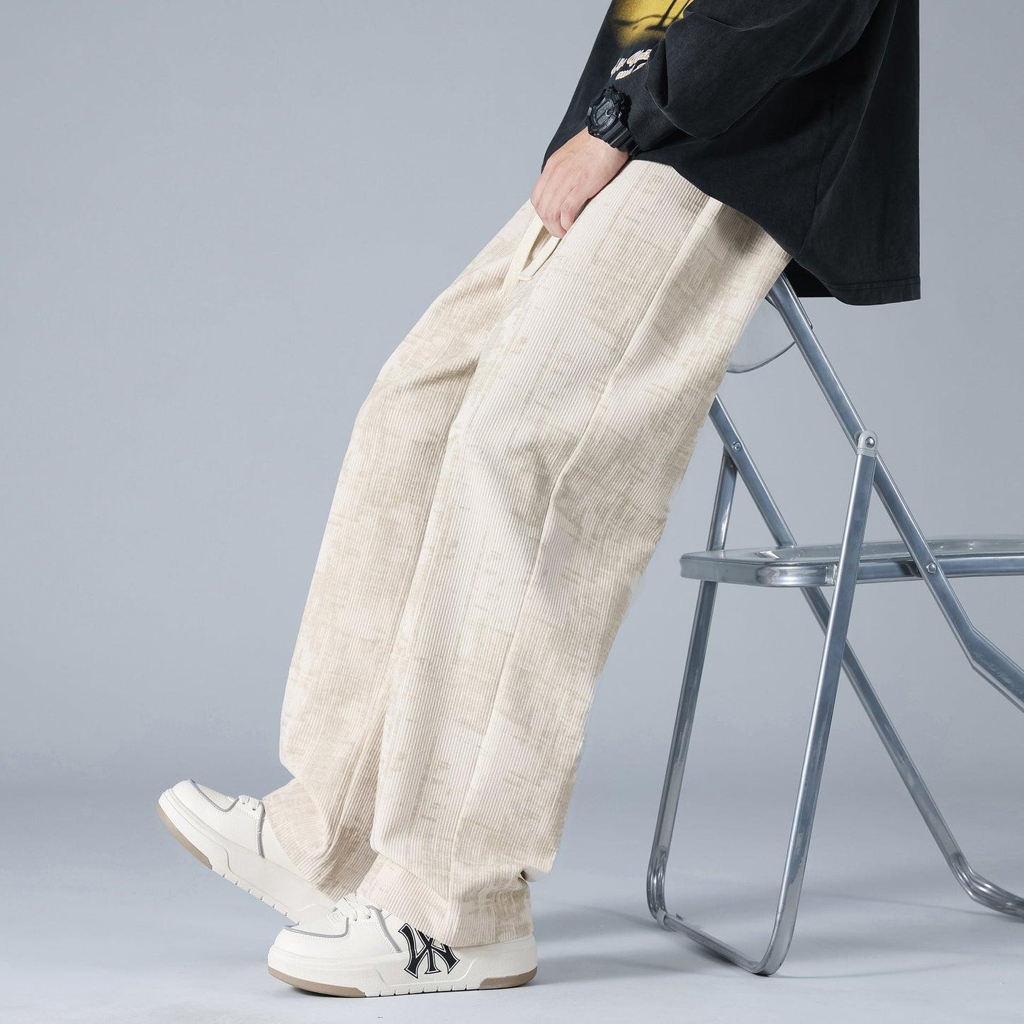 Pantaloni larghi beige su sedia pieghevole, abbinati a scarpe bianche con logo nero. Moda casual uomo, stile urbano contemporaneo.