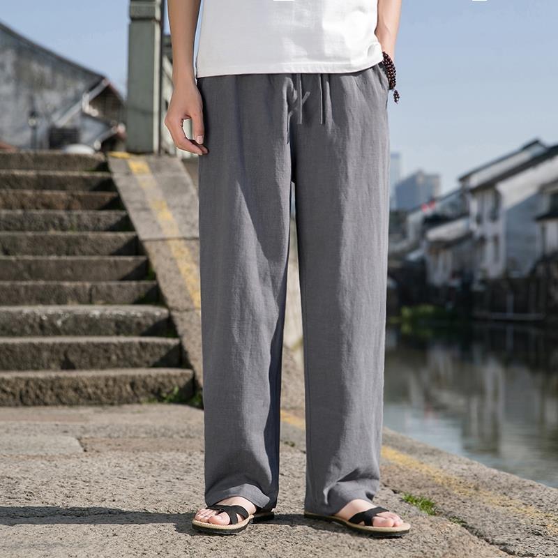 Uomo in pantaloni larghi grigi e sandali, in piedi su una strada acciottolata vicino a un canale. Moda casual estiva, stile urbano.