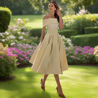 Donna in abito elegante color crema in un giardino fiorito, cammina sorridente su prato verde. Moda femminile, abbigliamento estivo, stile sofisticato.