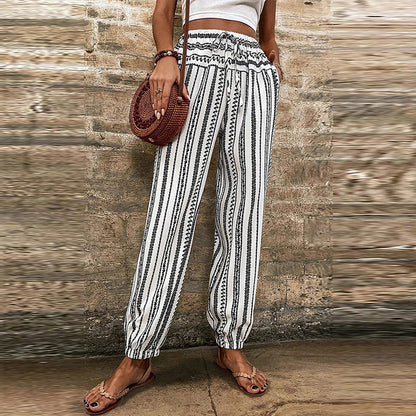 Pantaloni a righe bianche e nere con motivo etnico, indossati con sandali e borsa rotonda in paglia. Moda estiva casual donna.