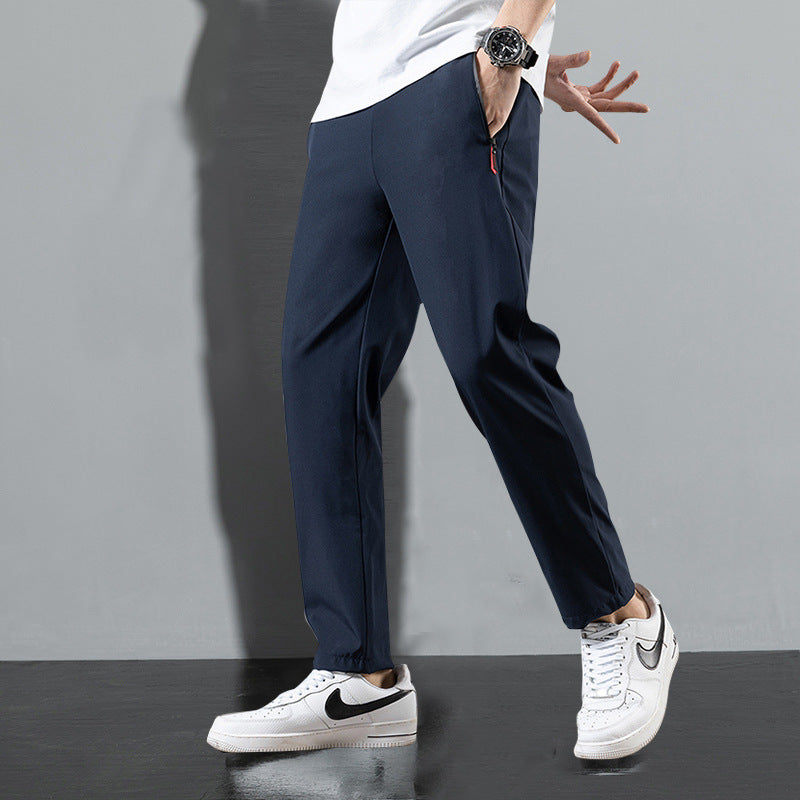 Pantaloni sportivi blu scuro da uomo, abbinati a scarpe da ginnastica bianche Nike, su sfondo grigio. Moda casual, abbigliamento maschile trendy.