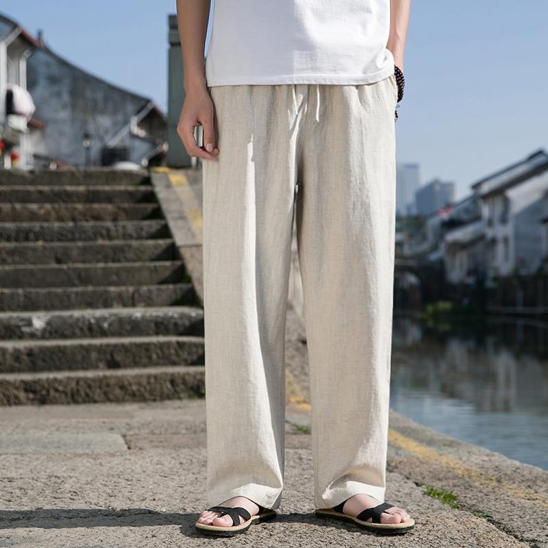 Uomo in pantaloni di lino beige e sandali neri su strada acciottolata vicino a canale, sfondo urbano. Moda estiva casual, comfort, stile rilassato.