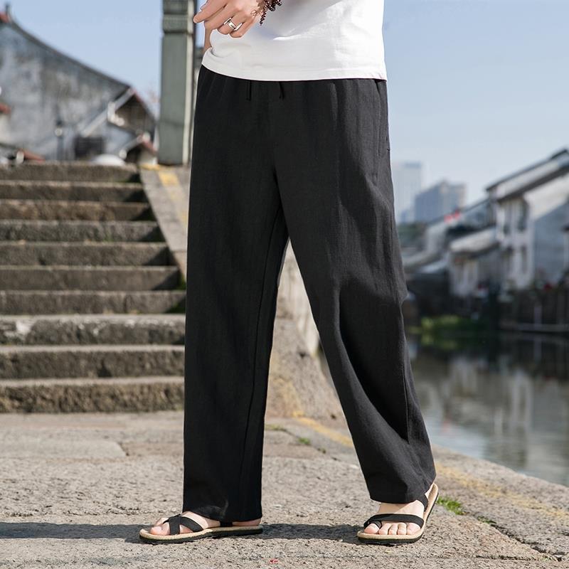 Pantaloni larghi neri da uomo, stile casual, indossati con sandali su strada acciottolata, sfondo urbano. Moda estiva, comfort, eleganza.