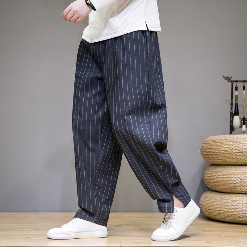 Pantaloni larghi a righe verticali blu scuro, stile casual, indossati con scarpe da ginnastica bianche su sfondo neutro. Moda uomo contemporanea.