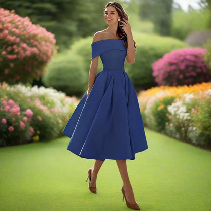 Donna in abito blu elegante in giardino fiorito, cammina su prato verde. Moda femminile, abbigliamento estivo, stile sofisticato.