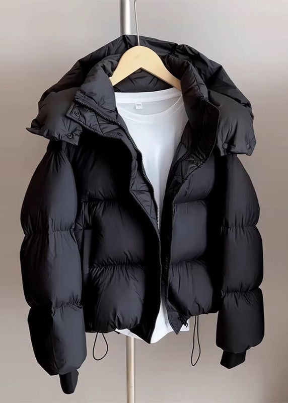 Giacca piumino nero con cappuccio su appendiabiti, sopra maglietta bianca. Moda invernale, abbigliamento caldo, stile casual.