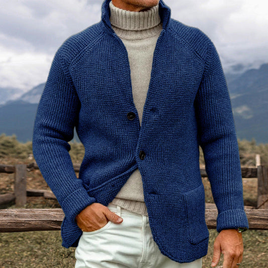 Uomo con maglione blu a maglia grossa e dolcevita beige, in un paesaggio montano. Moda invernale, abbigliamento caldo, stile casual elegante.