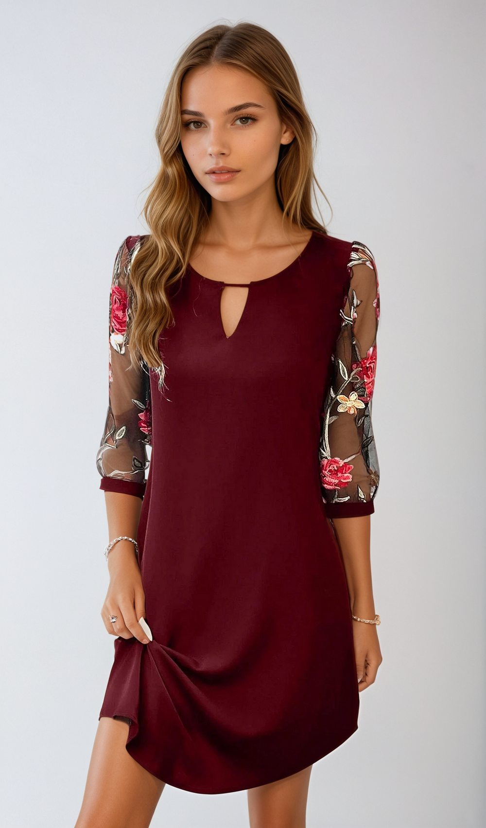 Giovane donna in abito bordeaux con maniche trasparenti ricamate a fiori, posa elegante. Moda femminile, abbigliamento elegante, tendenze 2023.