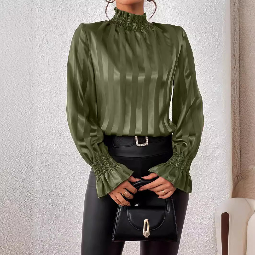 Donna con camicetta verde a righe verticali e pantaloni neri, tiene una borsa nera. Moda elegante, abbigliamento autunnale, stile sofisticato.