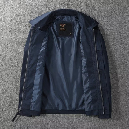 Giacca blu scuro da uomo aperta, con fodera interna in tessuto lucido, zip laterali, su sfondo grigio. Elegante e moderna, ideale per l'autunno.