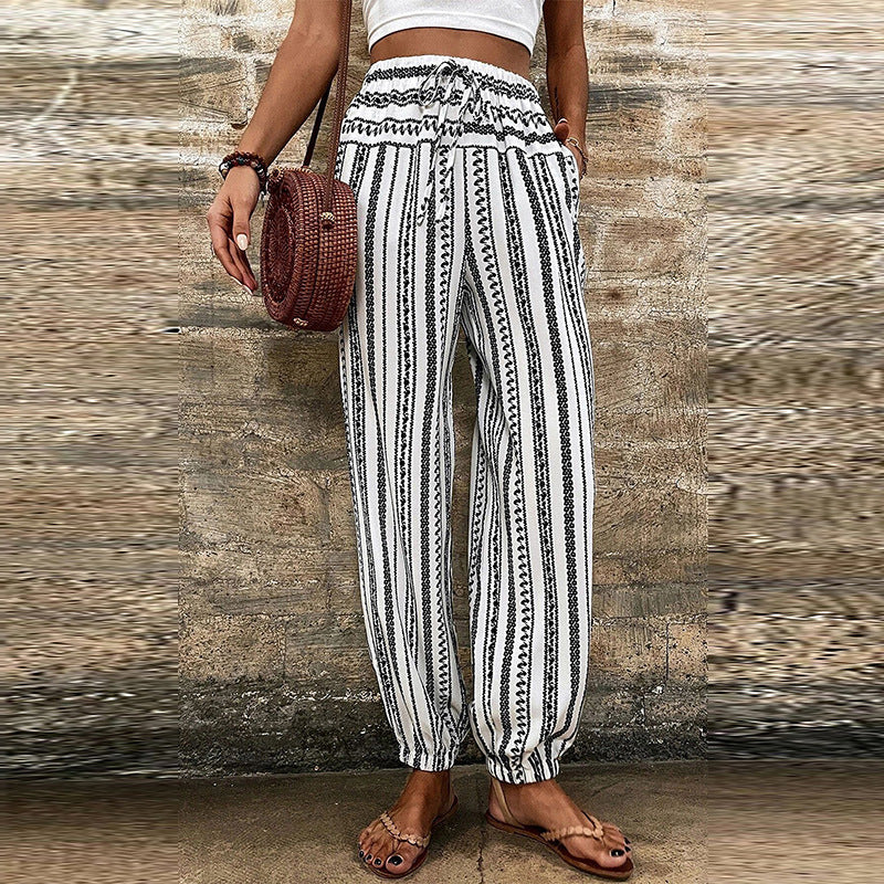 Pantaloni a righe bianche e nere con motivo etnico, indossati da una donna con sandali e borsa rotonda. Stile casual estivo, moda femminile.