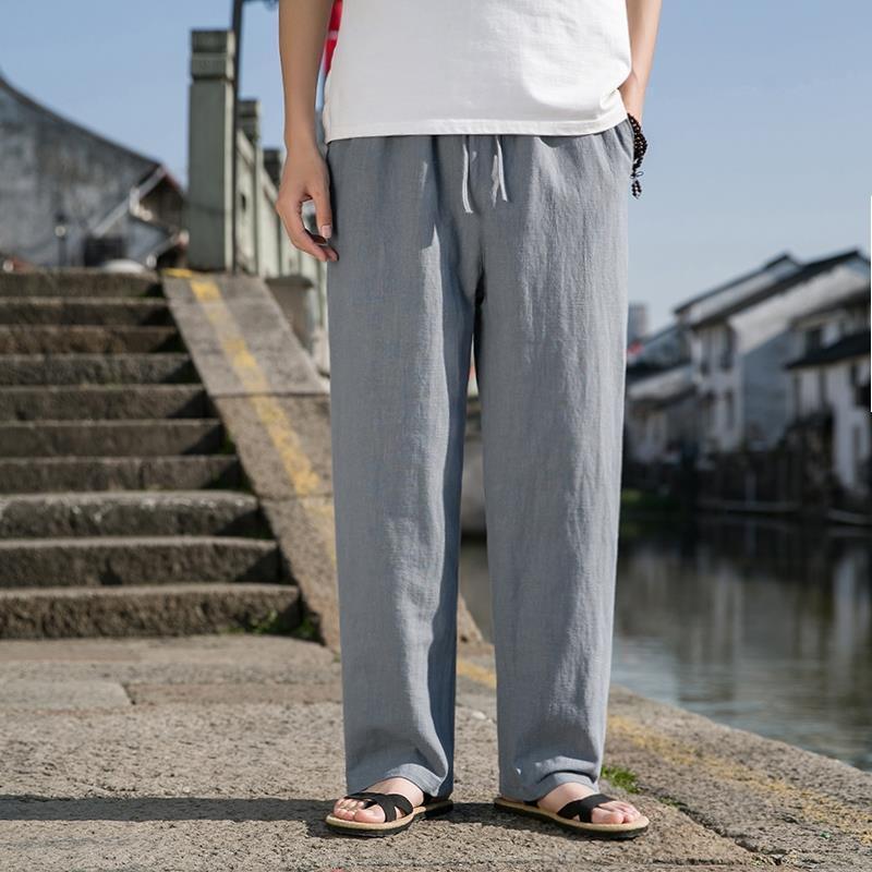 Uomo in pantaloni di lino grigi e sandali, vicino a un canale urbano. Moda estiva casual, abbigliamento maschile, comfort e stile.