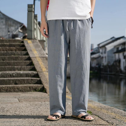 Uomo in pantaloni di lino grigi e sandali, vicino a un canale urbano. Moda estiva casual, abbigliamento maschile, comfort e stile.