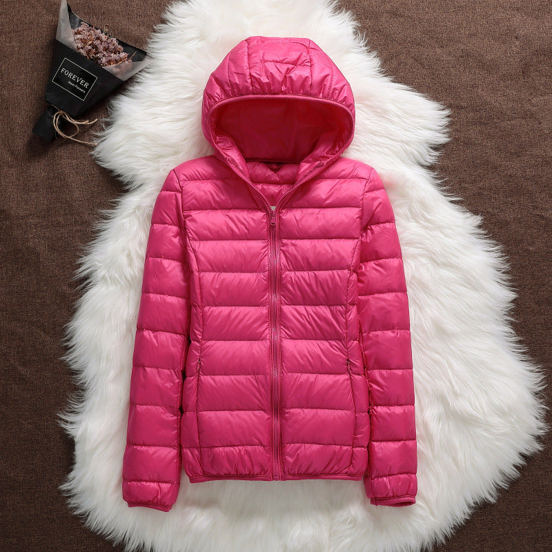 Giacca piumino rosa con cappuccio su tappeto bianco, moda invernale donna, abbigliamento caldo e leggero, stile casual elegante.