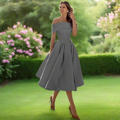 Donna in abito grigio elegante su prato verde, circondata da fiori rosa. Moda femminile, abbigliamento da cerimonia, stile sofisticato.