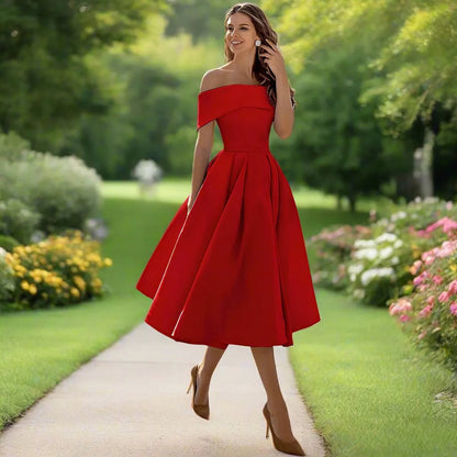 Donna in abito rosso elegante su sentiero di giardino fiorito, moda estiva, stile classico, abbigliamento femminile, natura verde, giornata soleggiata.