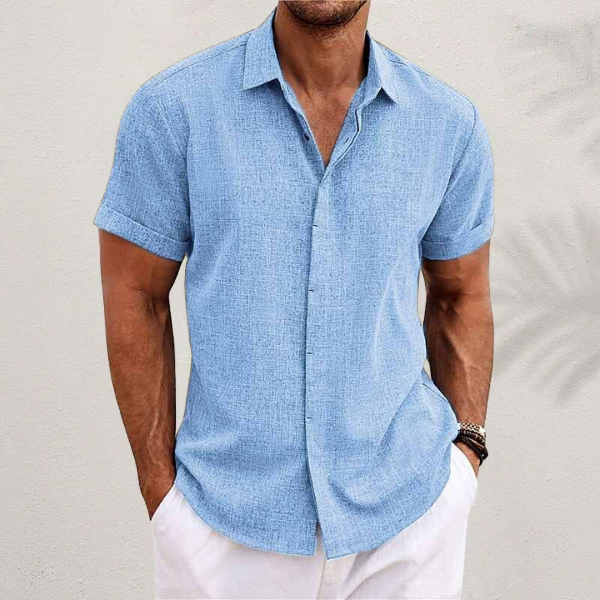 Camicia uomo estiva azzurra a maniche corte, tessuto leggero, abbinata a pantaloni bianchi. Look casual elegante per moda estiva maschile.