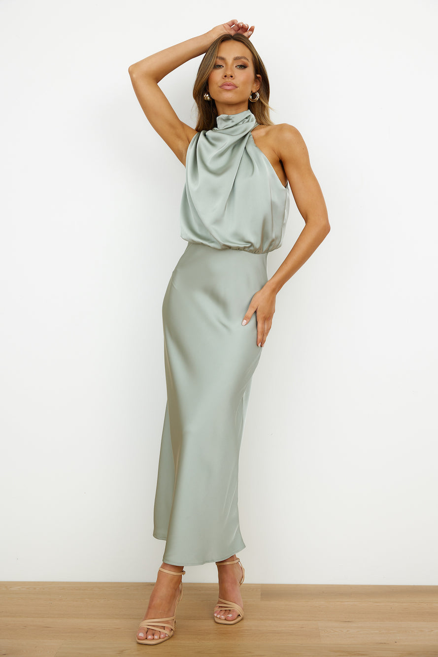 Donna in abito lungo di seta verde salvia, elegante e senza maniche, posa su sfondo bianco. Moda femminile, abbigliamento da sera chic.