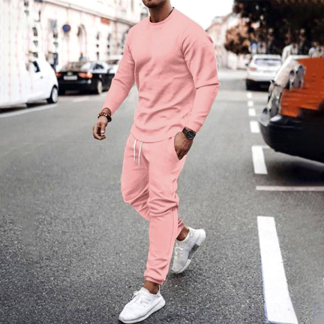 Uomo in tuta sportiva rosa, cammina su strada cittadina. Indossa scarpe da ginnastica bianche. Moda casual maschile, abbigliamento urbano.
