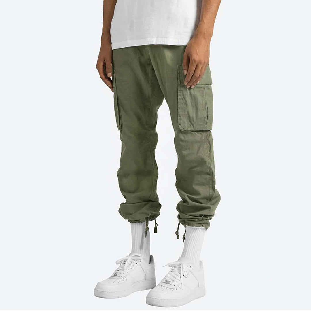 Pantaloni cargo verde oliva da uomo, tasche laterali, abbinati a scarpe da ginnastica bianche e calzini alti, moda casual urbana.