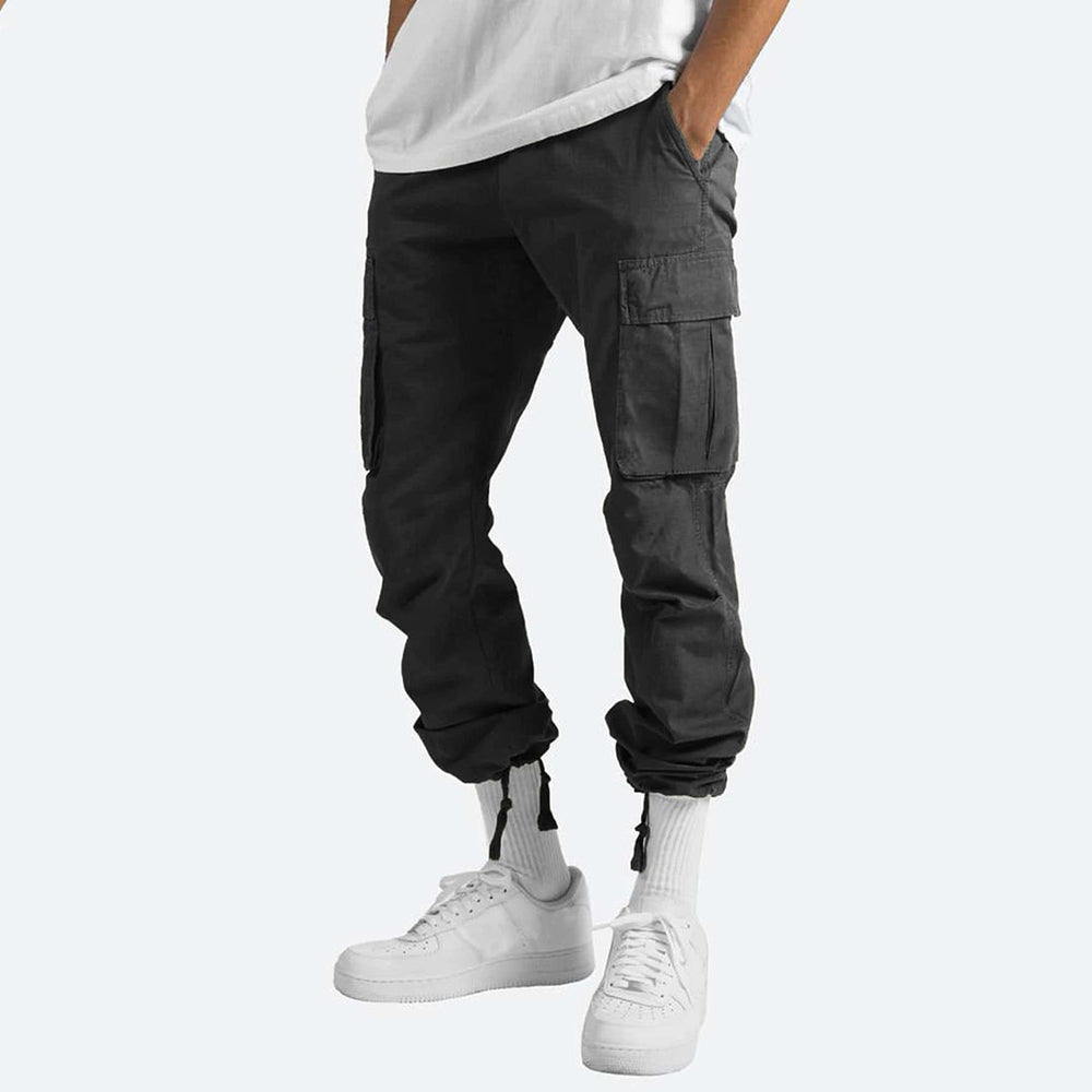 Pantaloni cargo neri da uomo, tasche laterali, abbinati a scarpe da ginnastica bianche e calzini alti. Stile casual moderno.