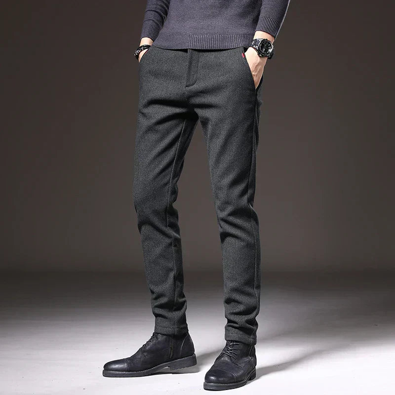 Pantaloni eleganti uomo grigio scuro, vestibilità slim, abbinati a maglione grigio e stivali neri. Moda maschile autunno-inverno.