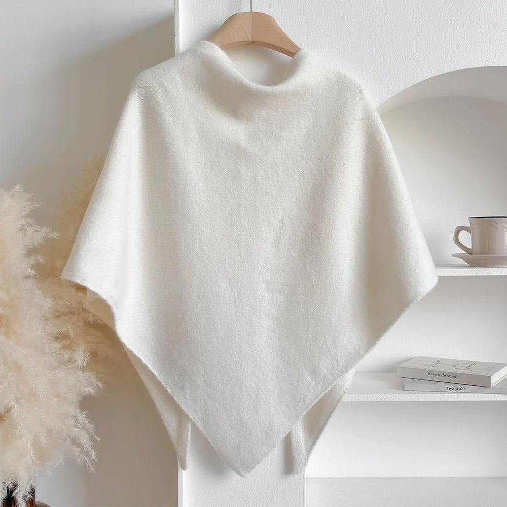 Poncho bianco in lana appeso su gruccia, design elegante e minimalista, ideale per moda autunno inverno, sfondo neutro con decorazioni leggere.