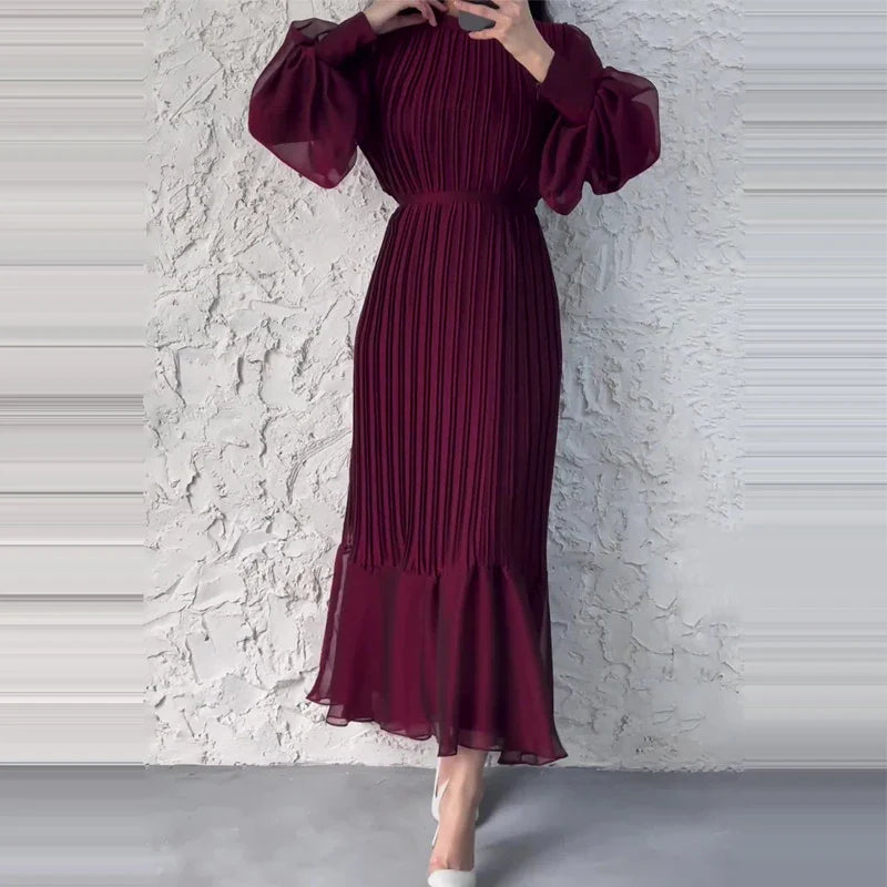 Abito lungo plissettato bordeaux con maniche a sbuffo, indossato da una donna su sfondo bianco. Elegante moda femminile, stile autunnale.