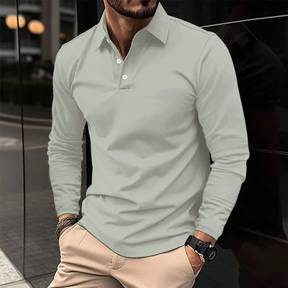 Uomo con camicia polo grigia e pantaloni beige, orologio nero al polso, posa casual in ambiente urbano. Moda maschile elegante e moderna.