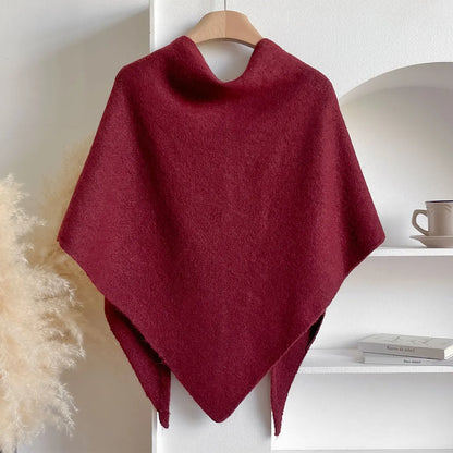 Poncho rosso in lana appeso su gruccia, sfondo bianco con scaffale e tazza. Moda autunnale, accessorio caldo ed elegante.