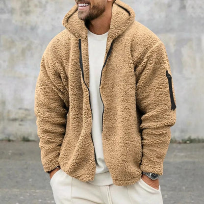 Uomo con giacca in pile beige, cappuccio e zip, su sfondo grigio. Moda casual invernale, abbigliamento caldo e confortevole.