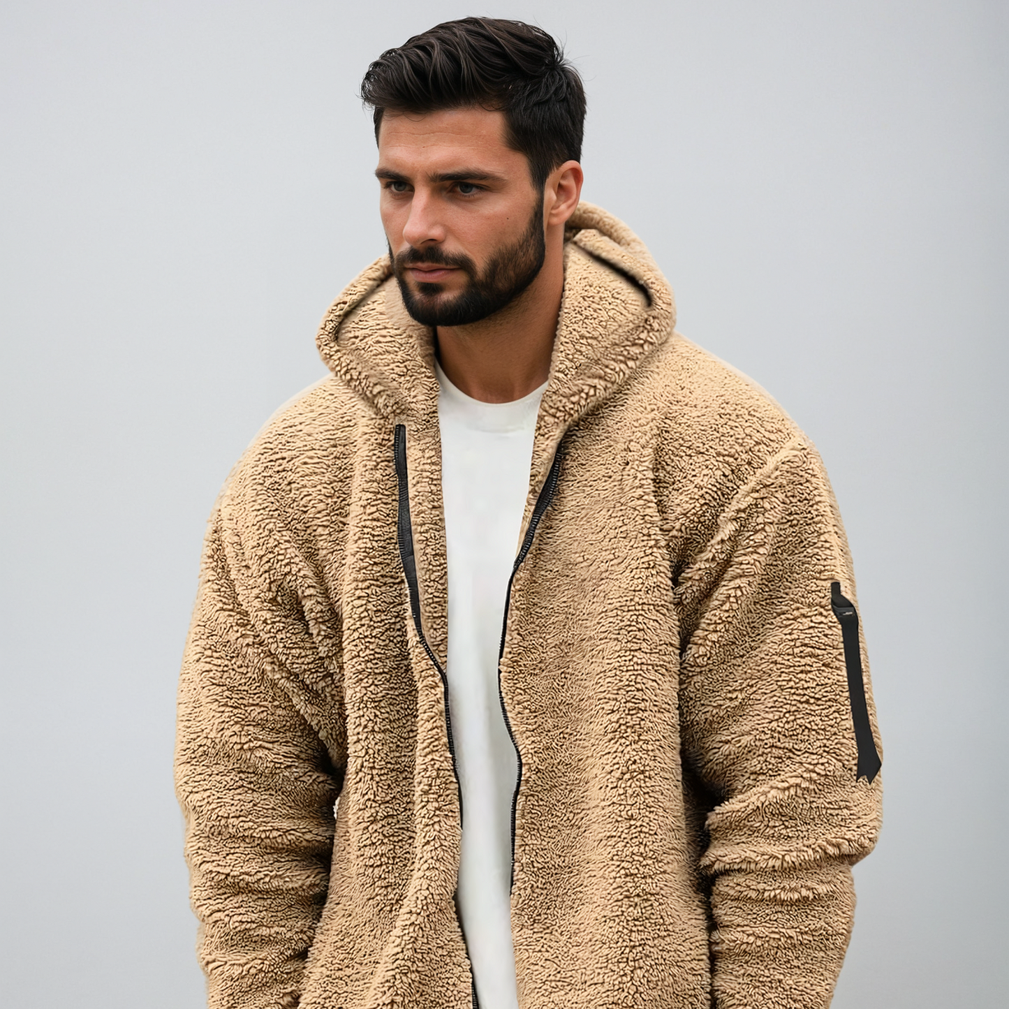 Uomo con giacca in pile beige, cappuccio e zip, su sfondo grigio. Moda autunnale, abbigliamento casual, stile moderno.