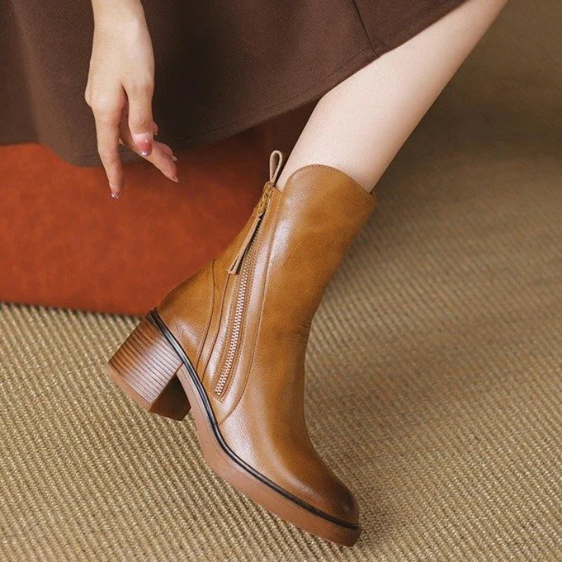 Stivaletti in pelle marrone con tacco largo, chiusura a zip laterale, indossati su tappeto beige. Moda autunnale, calzature eleganti donna.