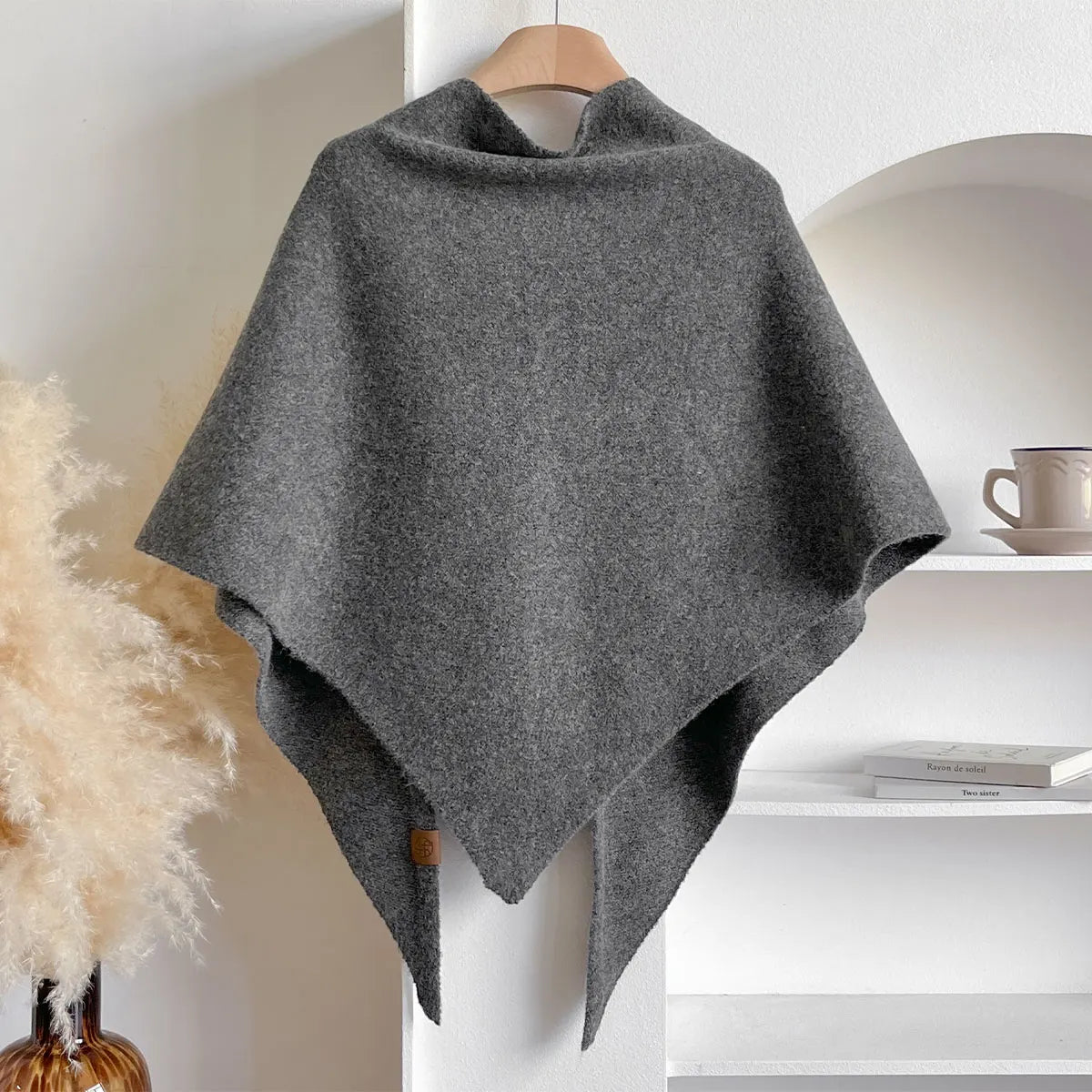 Poncho grigio in lana appeso su gruccia, design elegante e minimalista, perfetto per moda autunnale e invernale. Accessorio caldo e versatile.