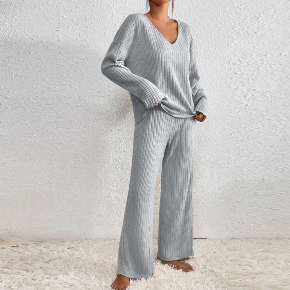 Donna in pigiama grigio a coste, maglia a maniche lunghe e pantaloni larghi, su tappeto bianco. Moda comoda, abbigliamento da casa elegante.