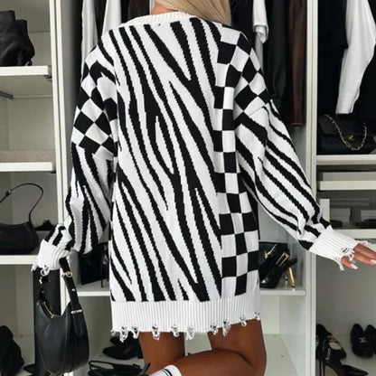 Donna con maglione oversize a righe e quadri bianco e nero, in piedi davanti a un armadio aperto con borse e vestiti. Moda autunnale, stile casual.