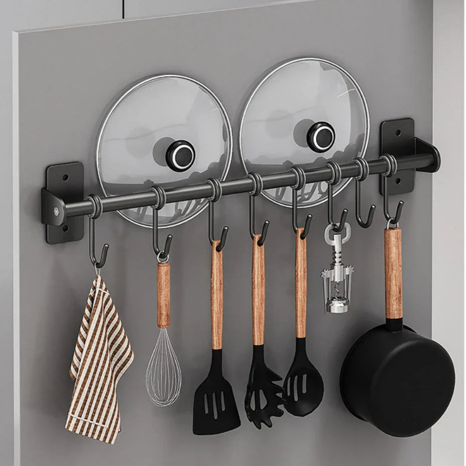 Porta utensili da cucina a parete con ganci, coperchi in vetro, mestoli in legno, frusta, presina a righe e padella nera. Organizzazione cucina.
