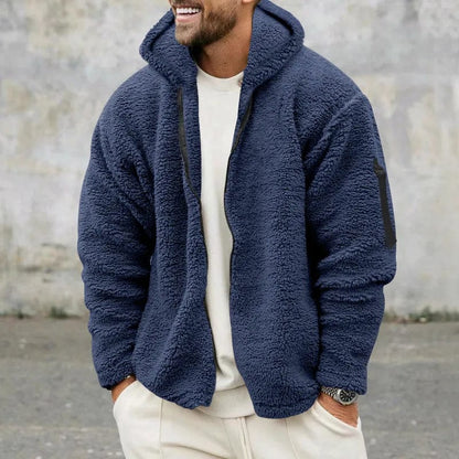 Uomo con giacca in pile blu, cappuccio e tasca sulla manica, sfondo grigio. Moda invernale, abbigliamento casual, stile confortevole.